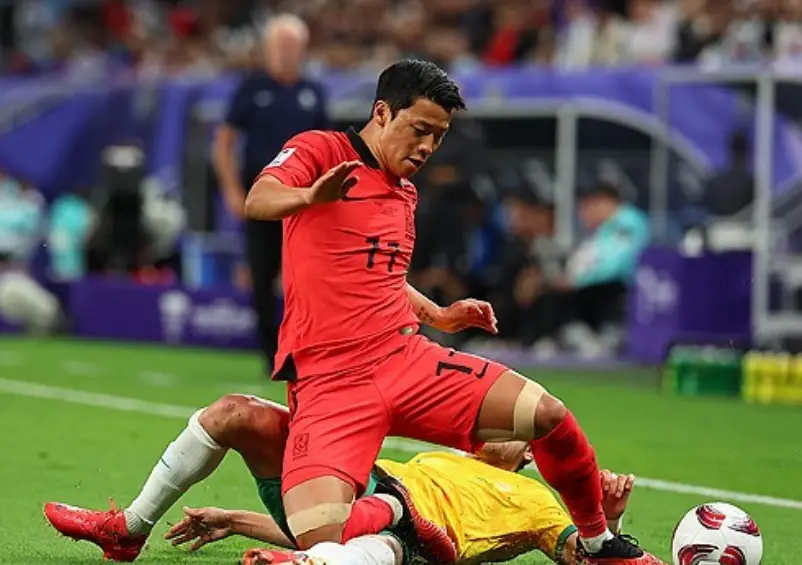 호주전- 축구장 그라운드에 누워있는 노란상의 초록 바지 호주선수와 그 위서 공을 향해 달려가는 붉은 유니폼 상하로 입은 황희찬