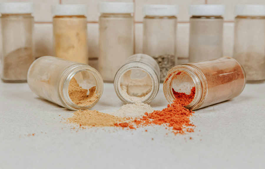 각종 조미료를 뚜껑이 있는 투명한 통에 담아서 뒤에 6개 놓고, 앞에는 뚜껑이 열린 조미료통 3개를 쓰러뜨려놓고 속에 있는 조미료를 흘려놓고 찍은 사진