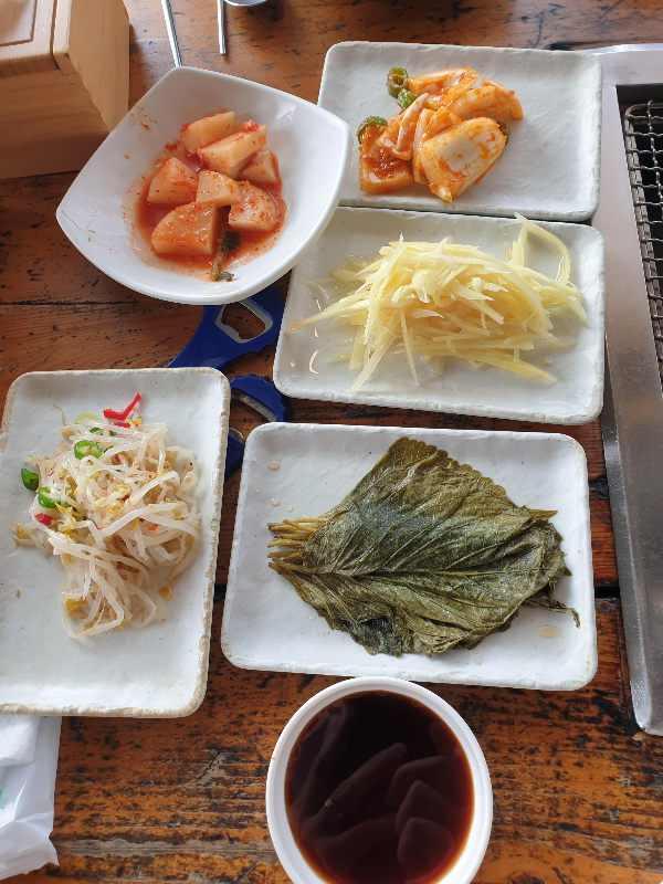 책상위에 숙주, 깍두기, 양파 무침, 생강, 깻잎, 간장이 올려져 있다.