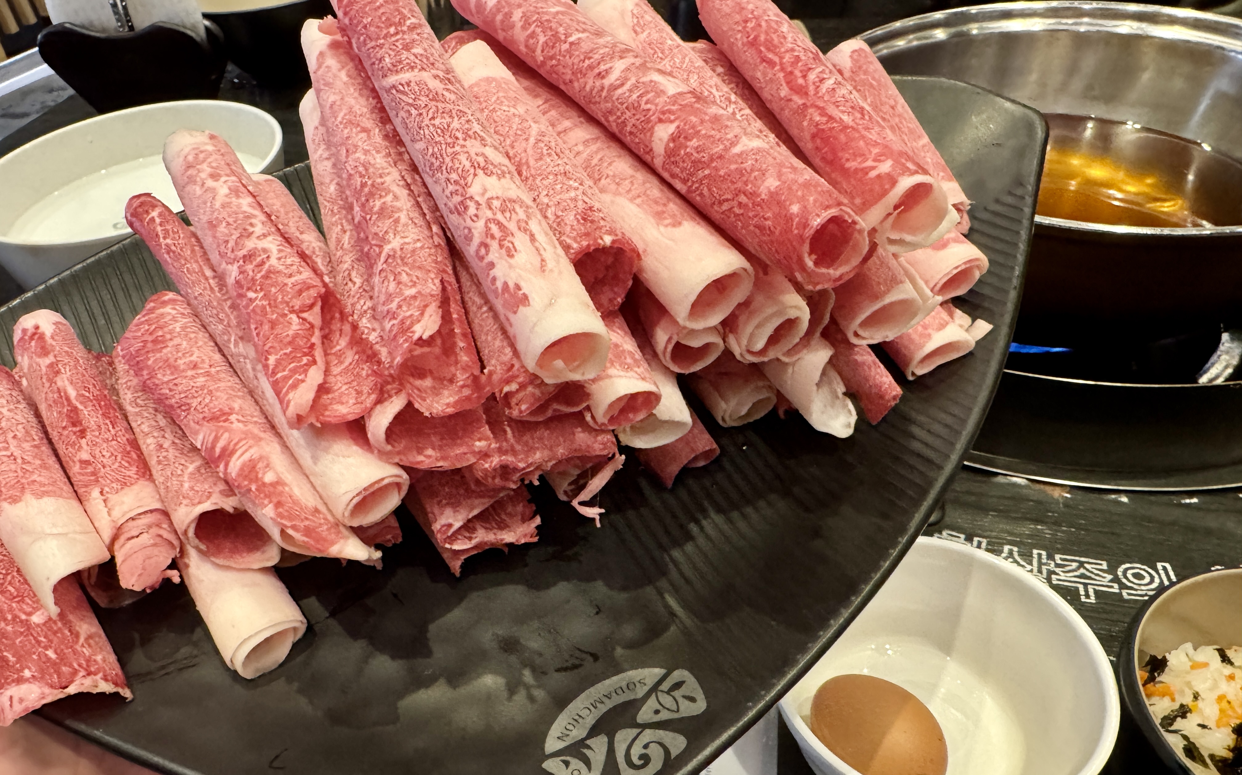 소담촌 김포한강신도시점에서 주문한 월남쌈 와규 샤브샤브 고기. 얇게 썰린 와규 소고기가 접시에 푸짐하게 담겨 있고, 뒷편에는 샤브샤브 국물 냄비와 계란, 밥이 함께 놓여 있어 가족 외식 메뉴로 인기 있는 조합을 보여준다.