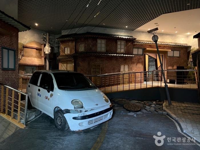 주택모형앞에 흰색 소형차 한대가 있다.