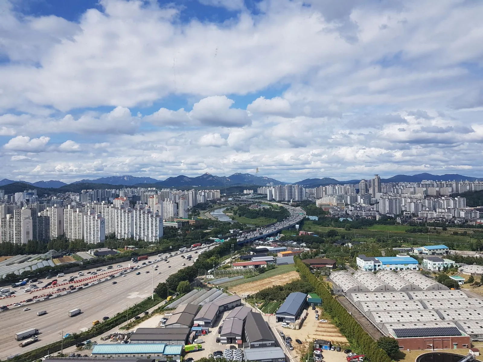 구리시의 공중 파노라마, 도시 스카이라인, 고속도로 및 구름 낀 하늘 아래의 산들.