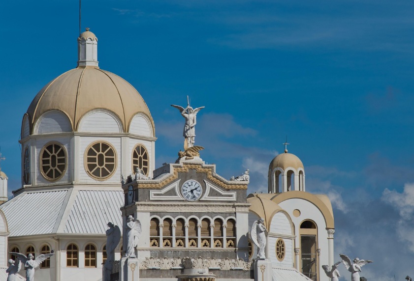 코스타리카 카르타고 로스 앙헬레스 대성당의 하얀색과 금색 돔, 정교한 천사 조각상과 중앙 시계탑이 돋보이는 건축물 전경