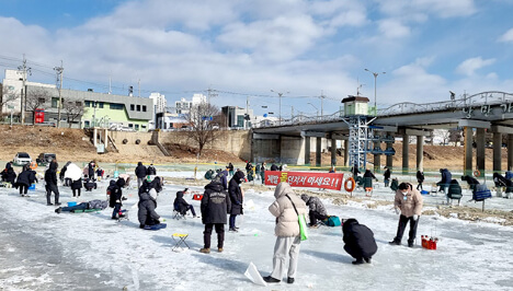 얼음 낚시터에서 사람들이 빙어와 송어를 낚기 위해 얼음 위에 의자를 두고 앉아 있는 모습과 겨울 축제의 활기찬 풍경