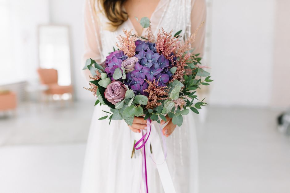 Close-up of a bride holding a beautiful bouquet featuring purple hydrangeas and roses.