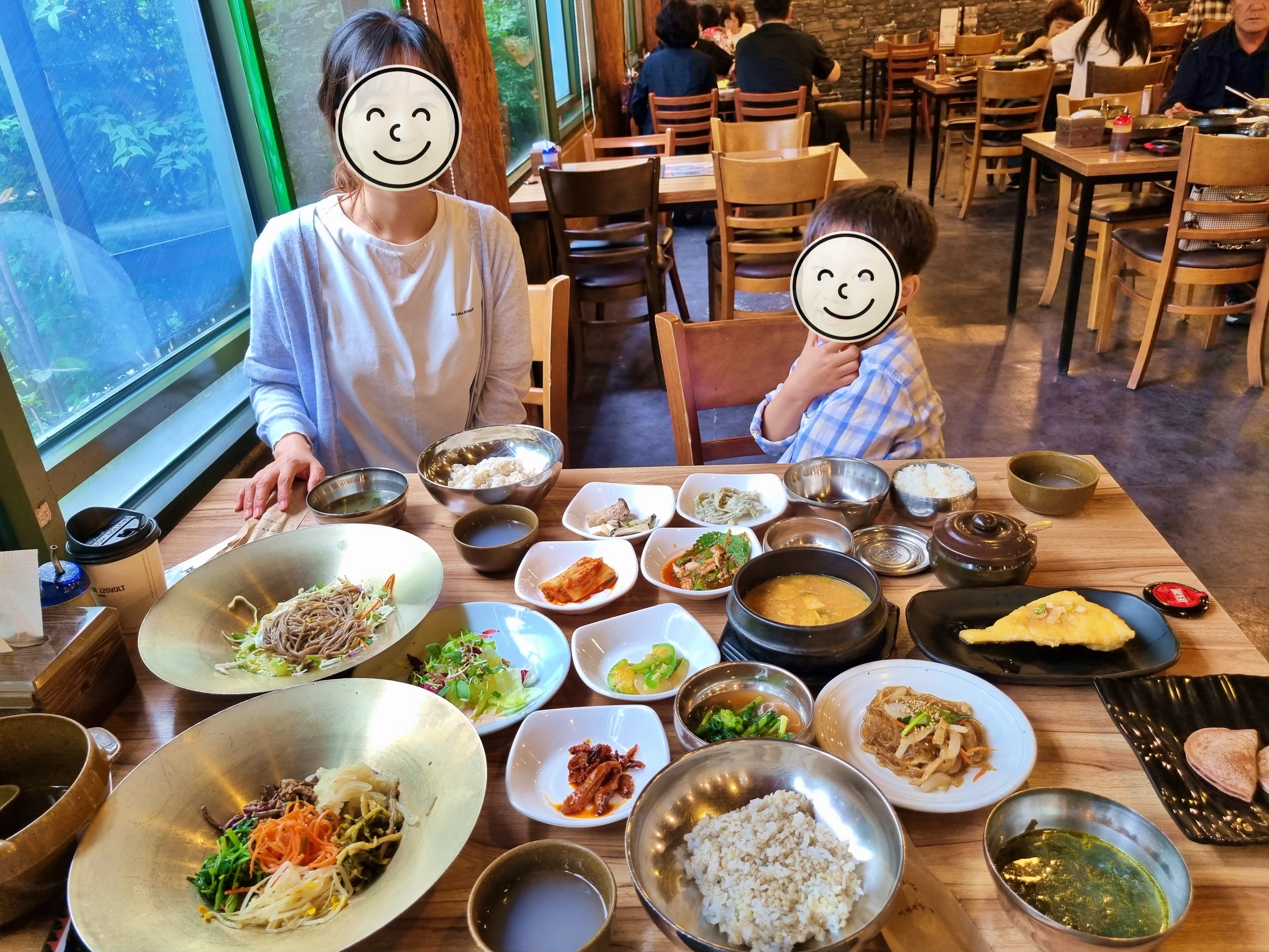 상위에 다양한 나물반찬과 생가튀김&amp;#44; 국&amp;#44; 보리밥 등이 있고 두사람이 앉아있다.