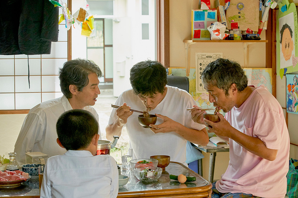 강변의 무코리타 연립주택에 사는 주민들이 함께 식탁에 모여 앉아 맛있는 음식을 함께 먹고 있는 모습