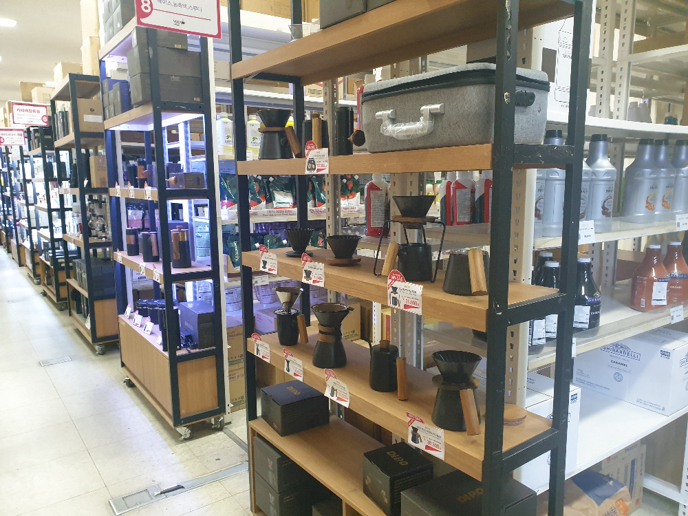 여러 렉들이 앞 뒤로 놓여있다. 각 렉에는 각종 커피 용품들이 놓여있다.