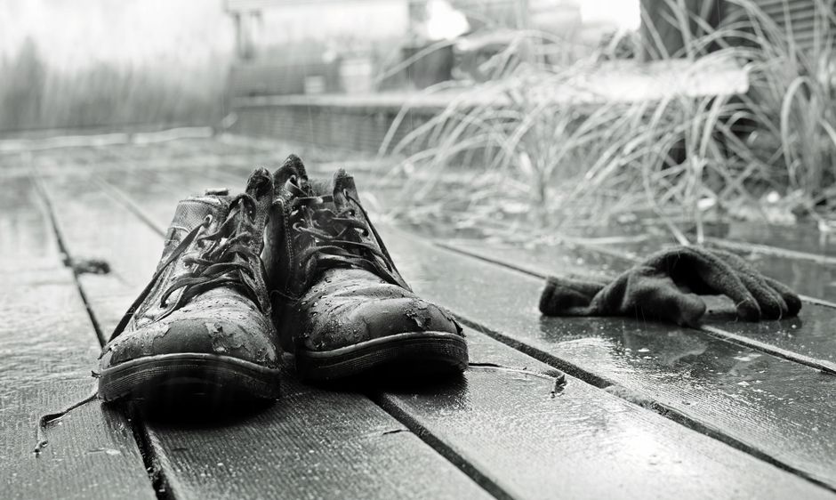 Black and white photo of wet shoes and gloves on a rainy wooden deck, conveying solitude.