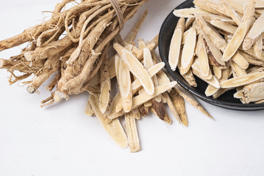 야생에서 채취를 한 황기 풀의 뿌리인 황기를 깨끗하게 세척하고 건조시킨 것을 하얀 바닥 위에 뿌리 채 두고 그 옆에는 황기를 편으로 잘라놓은 것을 검은 그릇과 바닥에 수북하게 놓아두고 찍은 사진