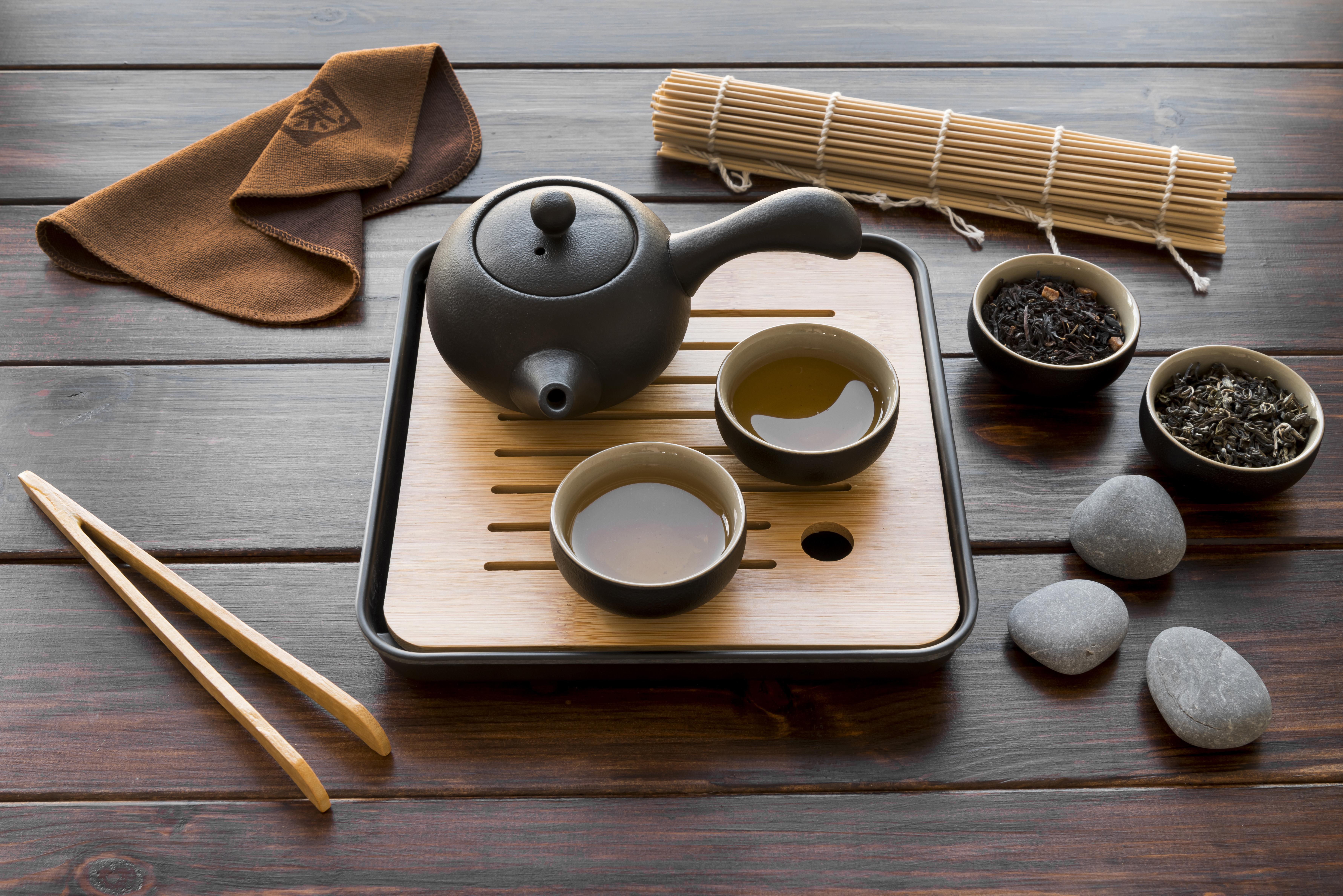고동색 나무바닥 위에 네모난 다기세트 위에 차주전자 1개와 차를 가득 담은 찻잔 2개를 두고 그 옆 바닥에 나무젓가락과 돌멩이 3개, 수건, 찻잎을 가득 담은 그릇 2개, 그리고 김밥말이를 두고 찍은 사진