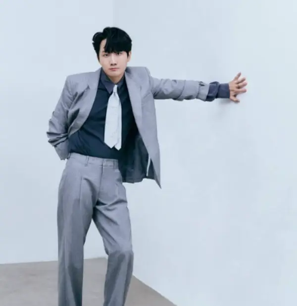 환승연애3- 파란색 벽에 회색 위아래 수트를 입고 남색셔츠에 흰넥타이를 매고 왼손을 뻗어 기대어 서있는 이용진