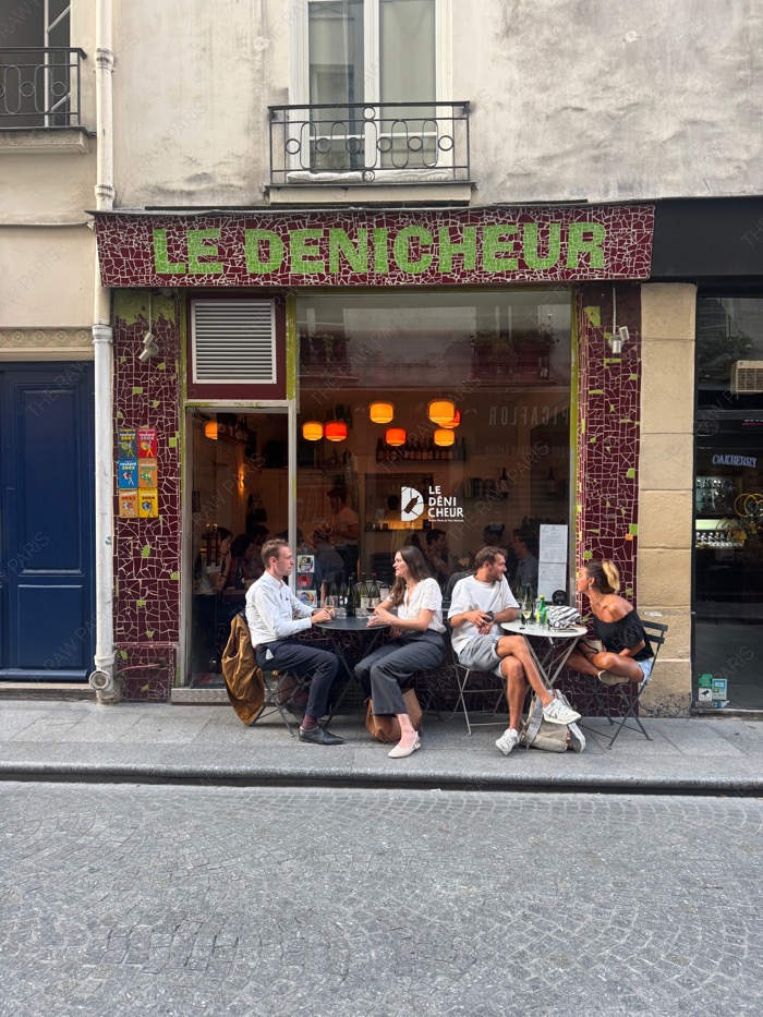 Exterior of Le Dénicheur wine bar in Paris with patrons drinking natural wine on the sidewalk terrace