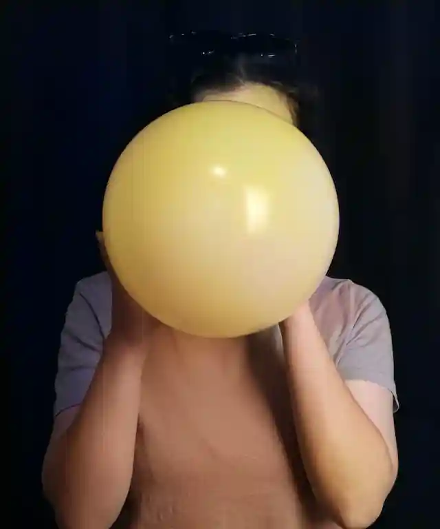 한 여성이 풍선을 힘껏 불고 있어서 풍선이 터지기 직전처럼 빵빵하게 부풀어 오르고 있다.