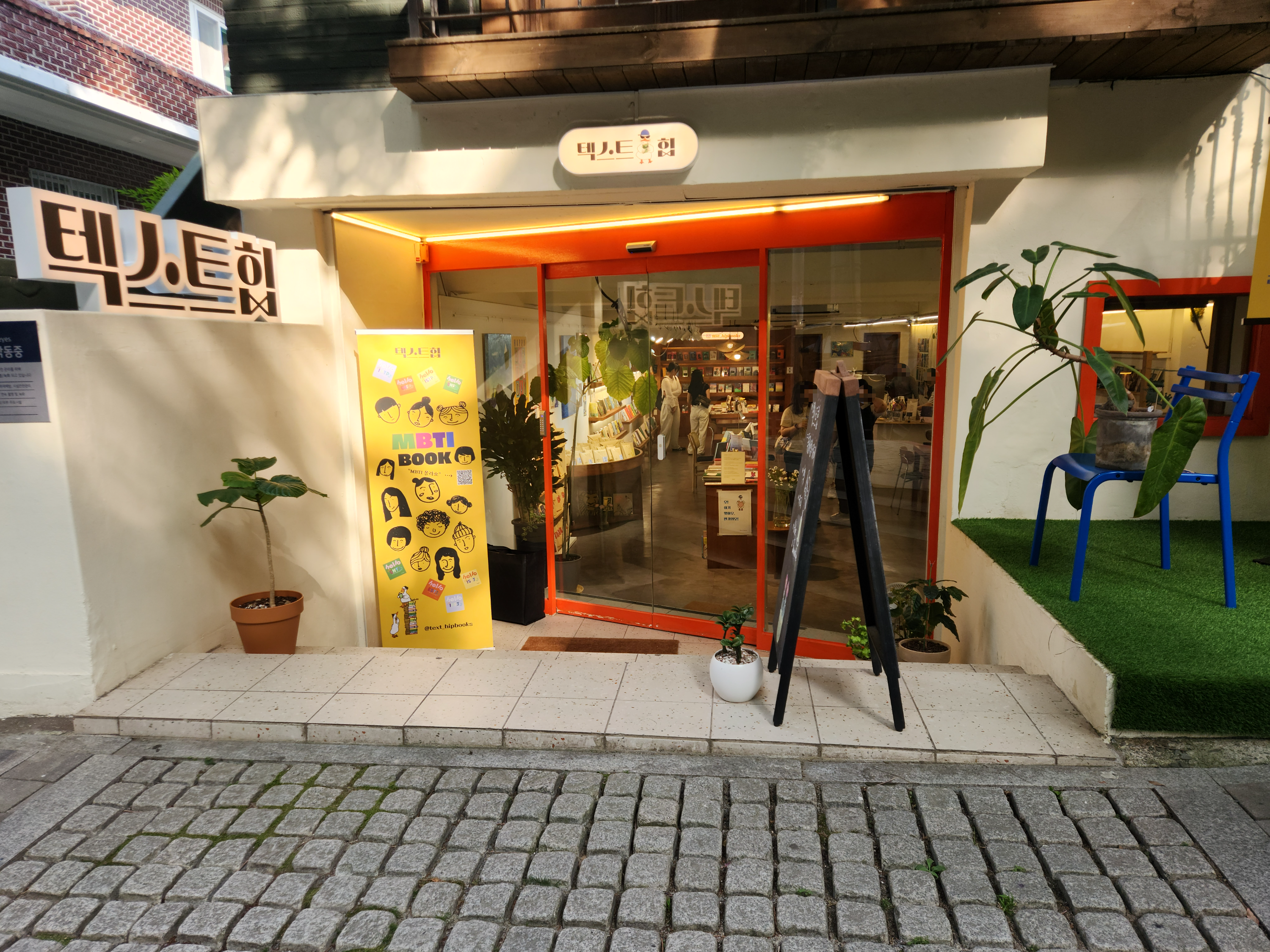 반지하 건물에 서점이 자리 잡고 있습니다. 서점 앞에는 간판과 판촉물&amp;#44; 잠시 쉬어 갈 수 있는 의자가 있습니다.