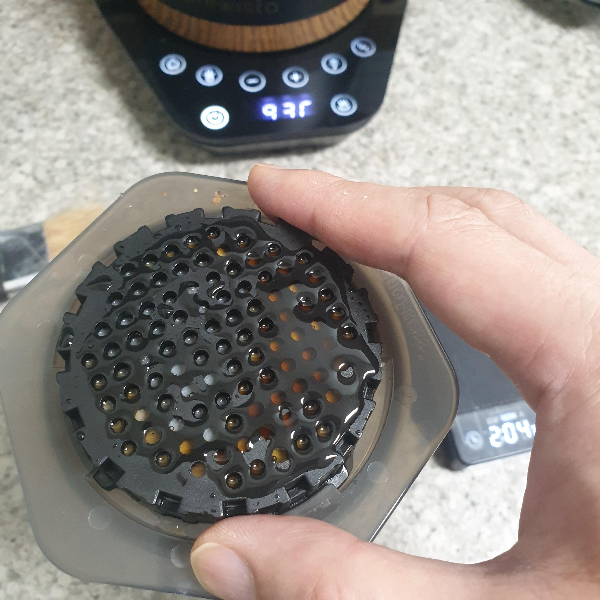 위쪽에 드립포트 하단부가 보임. 아래에 에어로스페스 필터캡을 잡고 천천히 아래로 누르는 모습