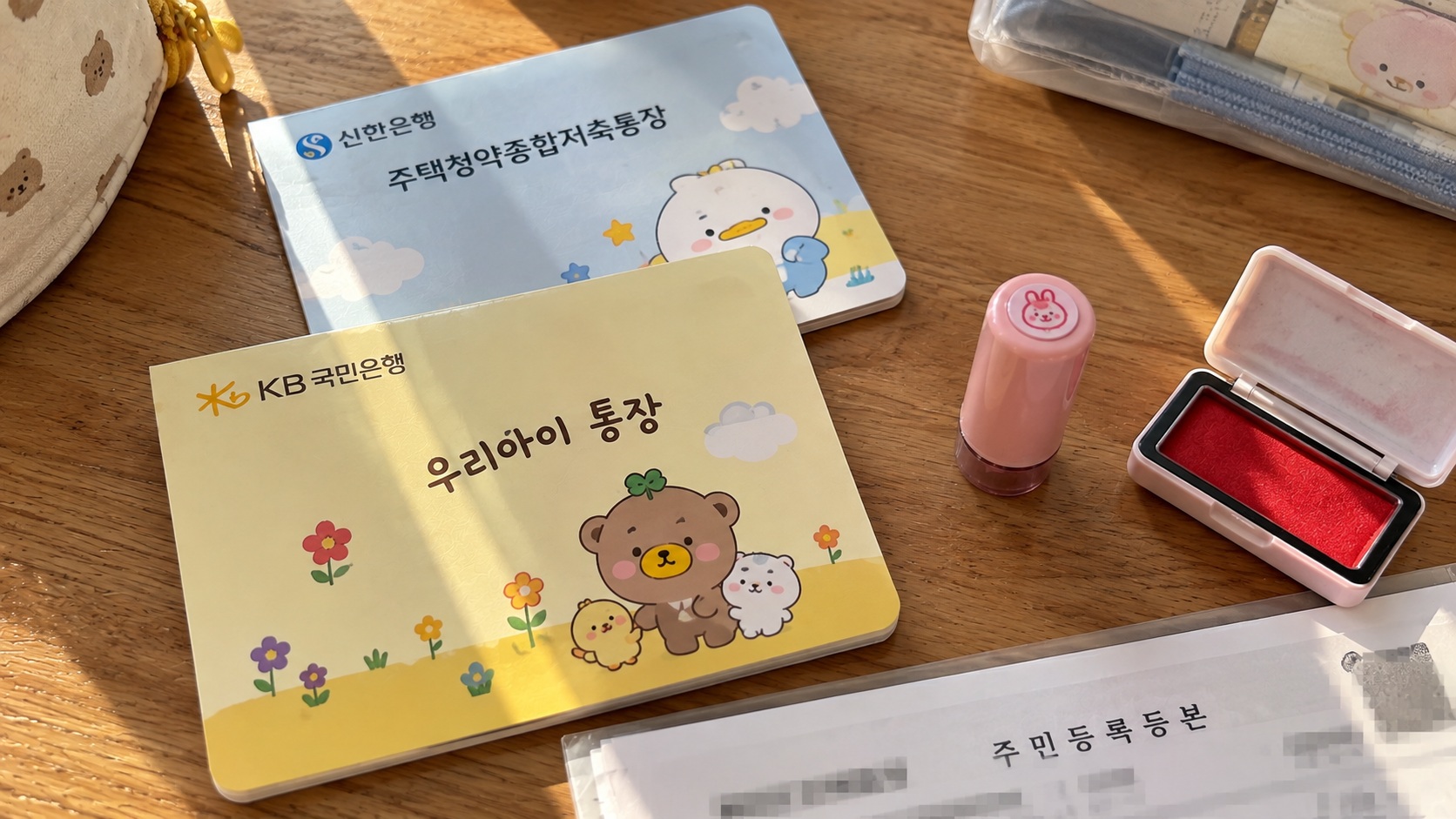원목 책상 위에 놓인 어린이 명의 통장과 주택청약종합저축통장, 도장 및 계좌변경 준비 서류
