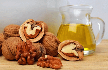 단단한 호두들이 있고 오른쪽엔 투명한 유리병에 노란색 호두기름이 가득 담겨있다.