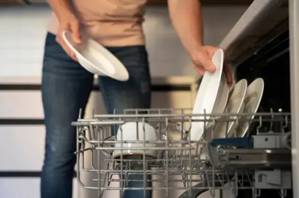 식기세척기에 접시를 정리하고 있는 사람의 모습, 그릇이 선반에 깔끔히 배열되어 있음