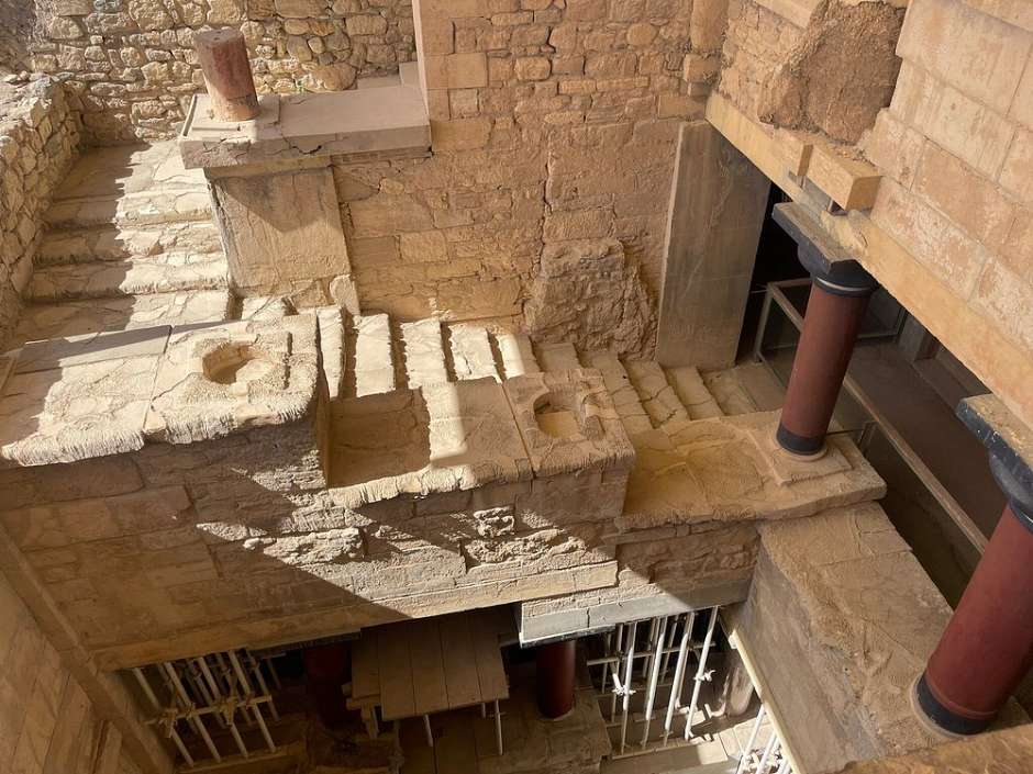 복원된 크노소스 궁전의 계단과 하부 공간. 여러 층으로 구성된 구조물과 미노아 양식 기둥이 특징적이다.