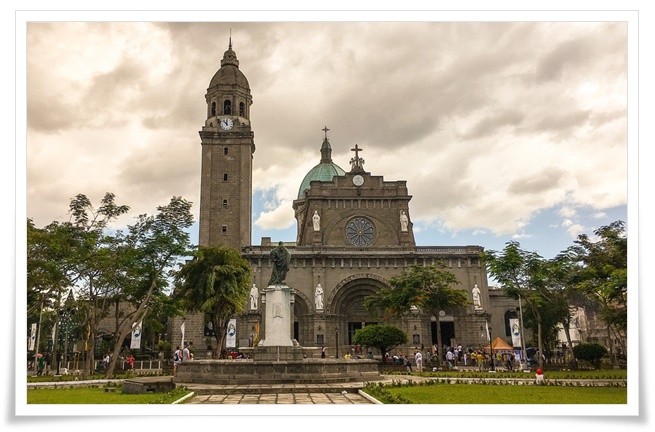 고딕양식의 거대한 종탑이 솟아있는 성당의 전경. 건물 앞 광장에는 사람들과 잘 관리된 정원이 펼쳐져 있다