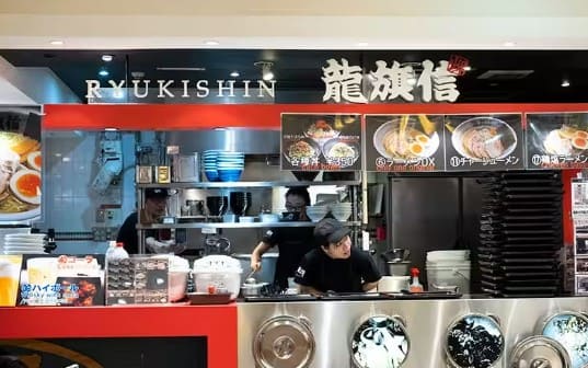 가게의 외부 사진 직원이 검은색 유니폼을 입고 매대에 기대어 밖을 보고 있다.