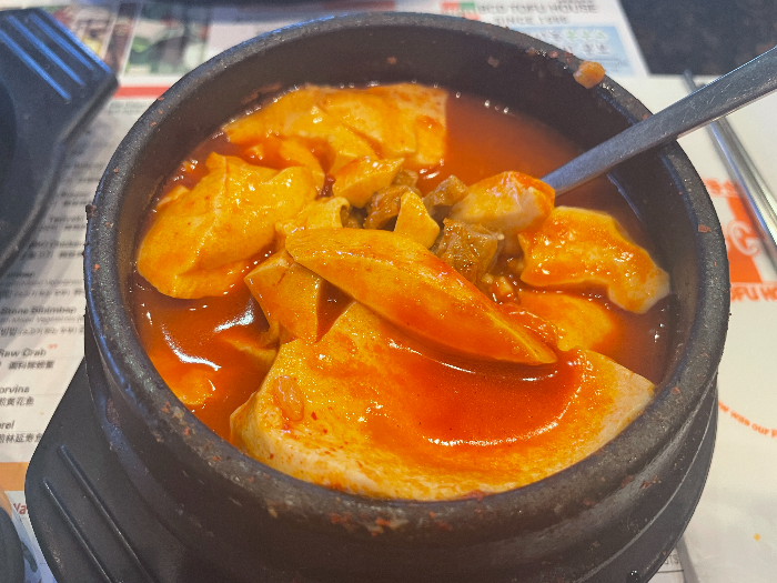 돌솥에 담긴 순두부 찌개. 빨간 국물에 하얀 순두부와 고기들이 들어 있다.