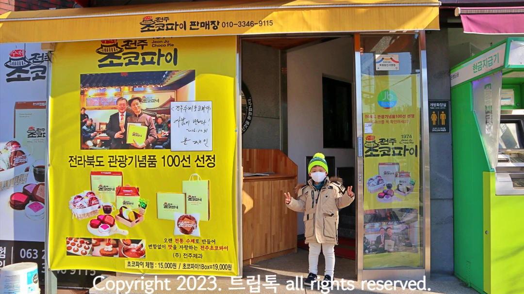 노란색벽면에 전주초코파이라고 써있는 입구 앞에 한 아이가 v자를 하고 서 있다.