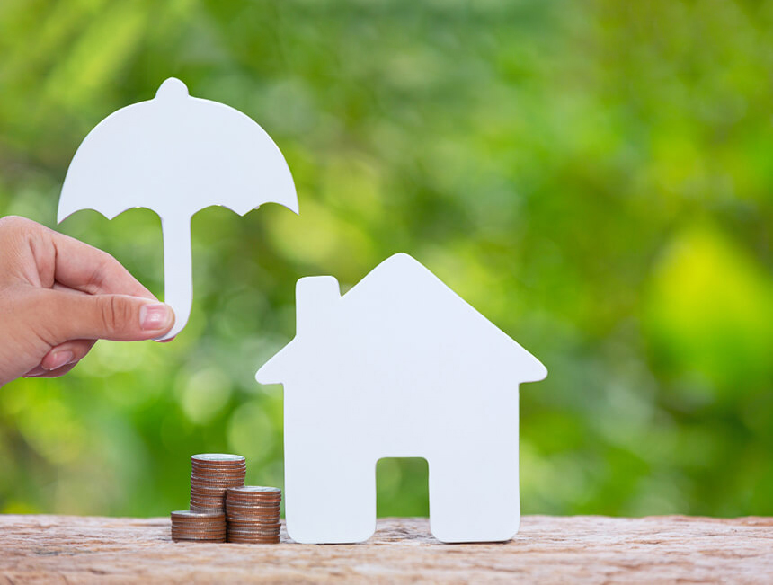 동전과 종이로 된 집 옆에 종이 우산을 들고 있는 손