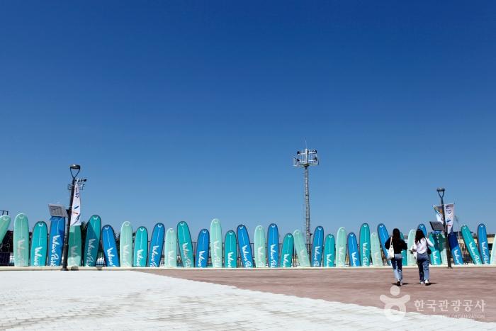 서핑보드 여러개가 세워져있고 그 앞으로 두 여자가 걸어가고 있다.