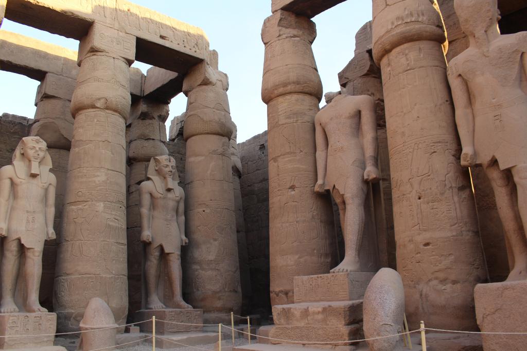 룩소르 신전 내부에 서 있는 여러 개의 대형 파라오 석상과 파피루스 양식의 기둥들. 기둥과 벽에는 고대 이집트의 부조가 새겨져 있다.