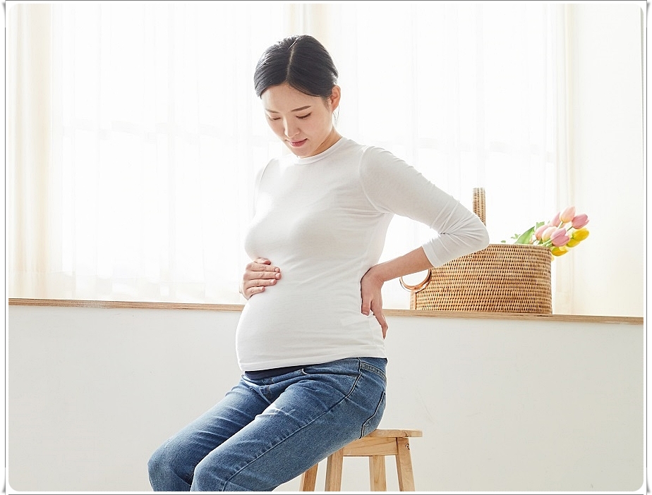배와 허리 부위를 손으로 감싸고 있는 임산부의 모습