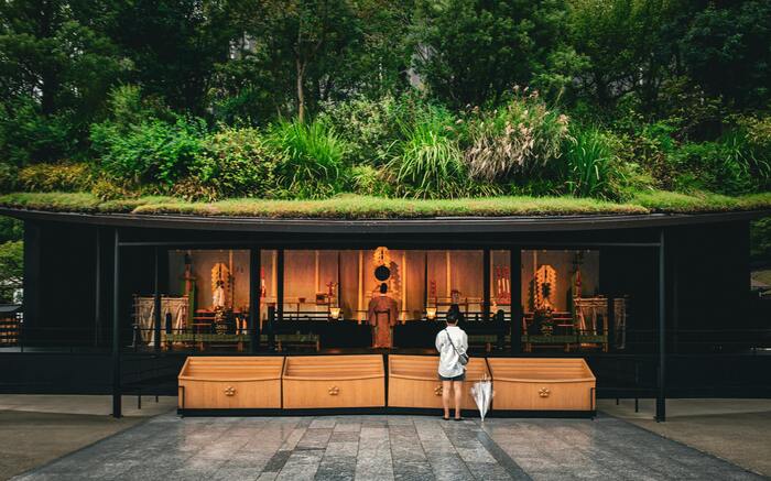 자연 속 전통 사찰 건물 앞에서 기도 중인 사람의 모습, 후쿠오카의 조용한 명소