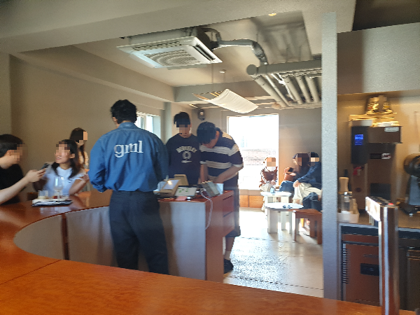 바 테이블에 고객이 앉아 있다. 주문하는 곳에서는 두명의 남성 고객이 바리스타에게 주문을 하고 있다.