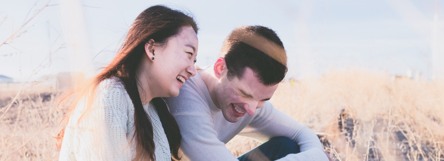 동양 여성과 서양 남성이 풀밭에 앉아서 환하게 웃고 있는 사진