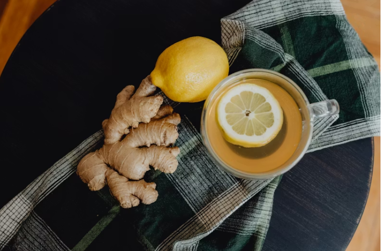 생강, 레몬, 레몬 슬라이스가 띄워진 따뜻한 차 한 잔이 테이블 위에 놓여 있는 모습