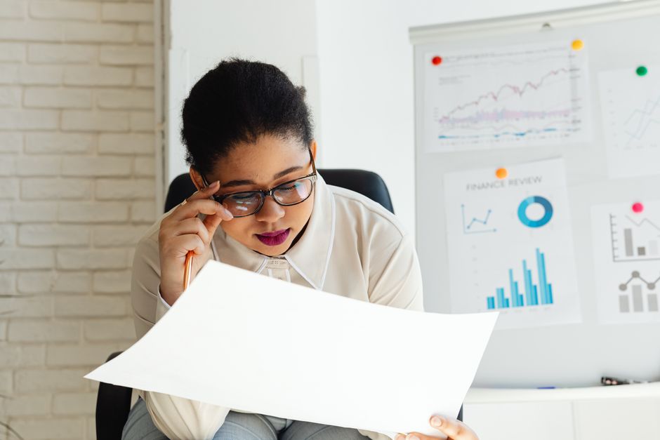 Focused businesswoman examining financial reports with graphs and charts on a whiteboard.