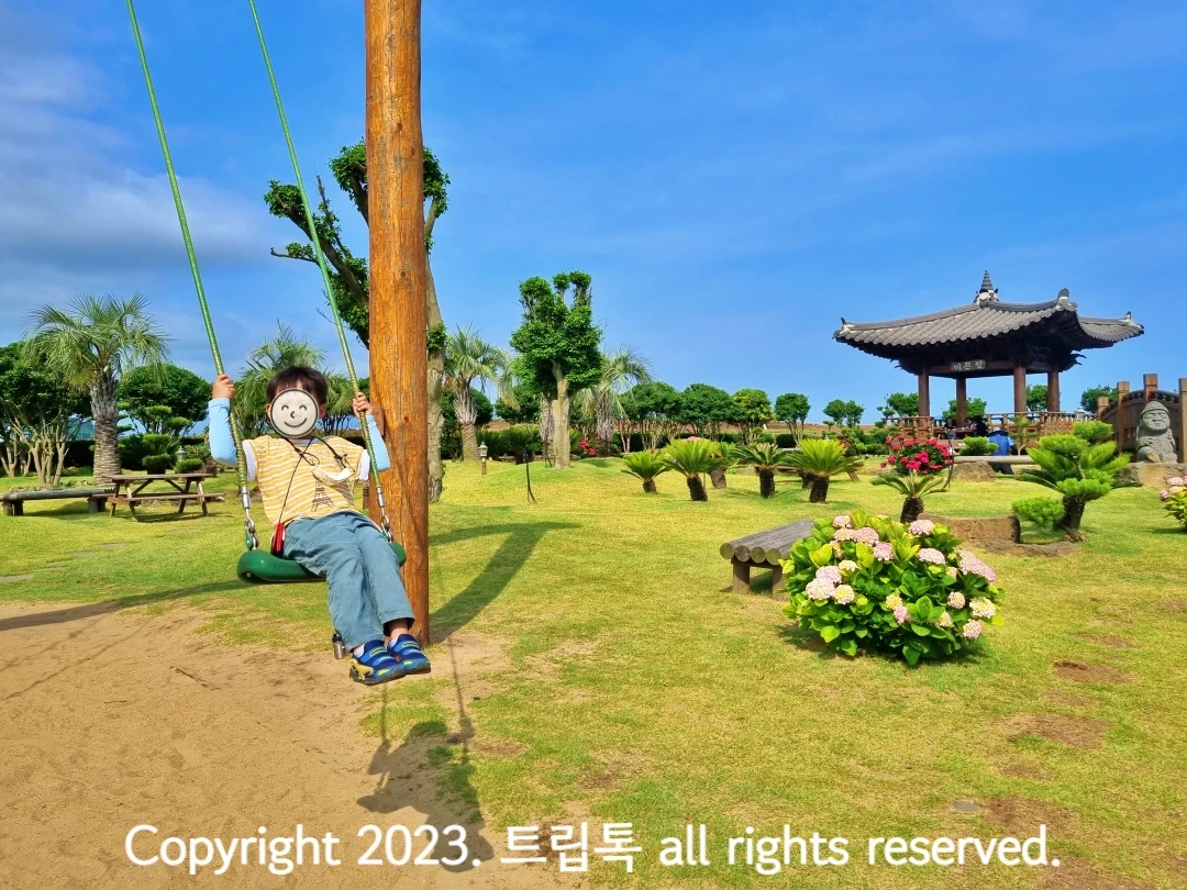 그네를 타고 있는 아이와 그 너무 연보라색 수국과 정자와 야자나무가 있는 넓은 정원이다