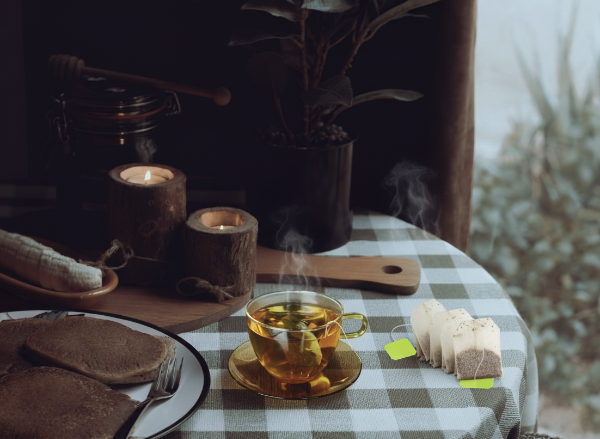 둥근 테이블 위에 양초 2개 빵 찻잔 그리고 티백이 놓여있다.