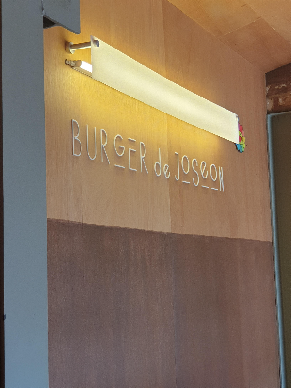 내부 조명과 로고, 나무 벽면에 간접조명이 설치되어 있고 그 아래 로고가 있다.