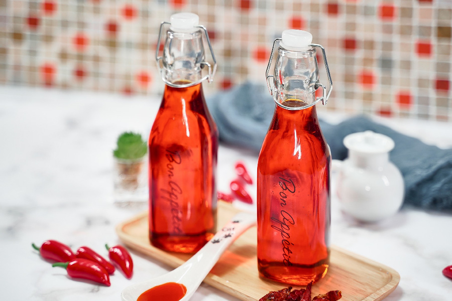 야생에서 채취를 한 고추를 기름을 넣어 볶은 후에 나온 기름을 투명한 유리병에 담은 것을 하얀 바닥 위에 네모난 나무 깔판 위에 2병을 놓아두고 그 옆에 작은 고추를 몇개 놓아두고 찍은 사진