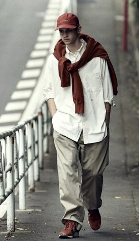 브라운 컬러의 볼캡&#44; 브라운 컬러의 신발&#44; 화이트 컬러 셔츠에 베이지 컬러 슬랙스를 매치한 시티보이룩에서 어깨에 브라운 컬러맨투맨을 걸침으로써 포인트를 준 코디 사진이다.