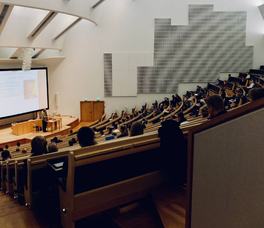 돔 형태의 대형 강의실에 많은 사람이 앉아있고 가장 앞에서는 한명의 남자가 강의하고 있다
