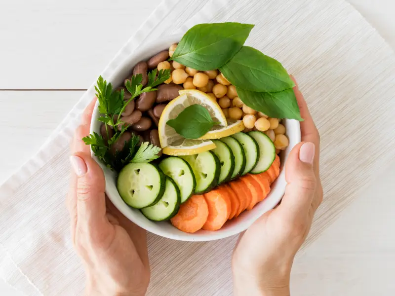 견과류 옥수수 오이 당근 푸른잎채소 등이 담겨 있는 흰그릇을 두손으로 들고 있는 다이어트 음식