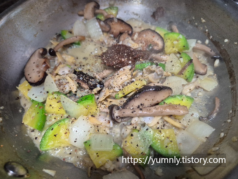 Grinding fresh black pepper over the Korean soybean paste (doenjang) in the pan.