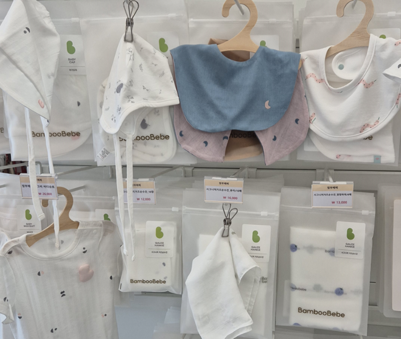 "아기용 턱받이와 모자 등 신생아 용품이 진열된 매장 진열대, 부드럽고 친환경 소재의 베이비 제품을 소개하는 장면"
