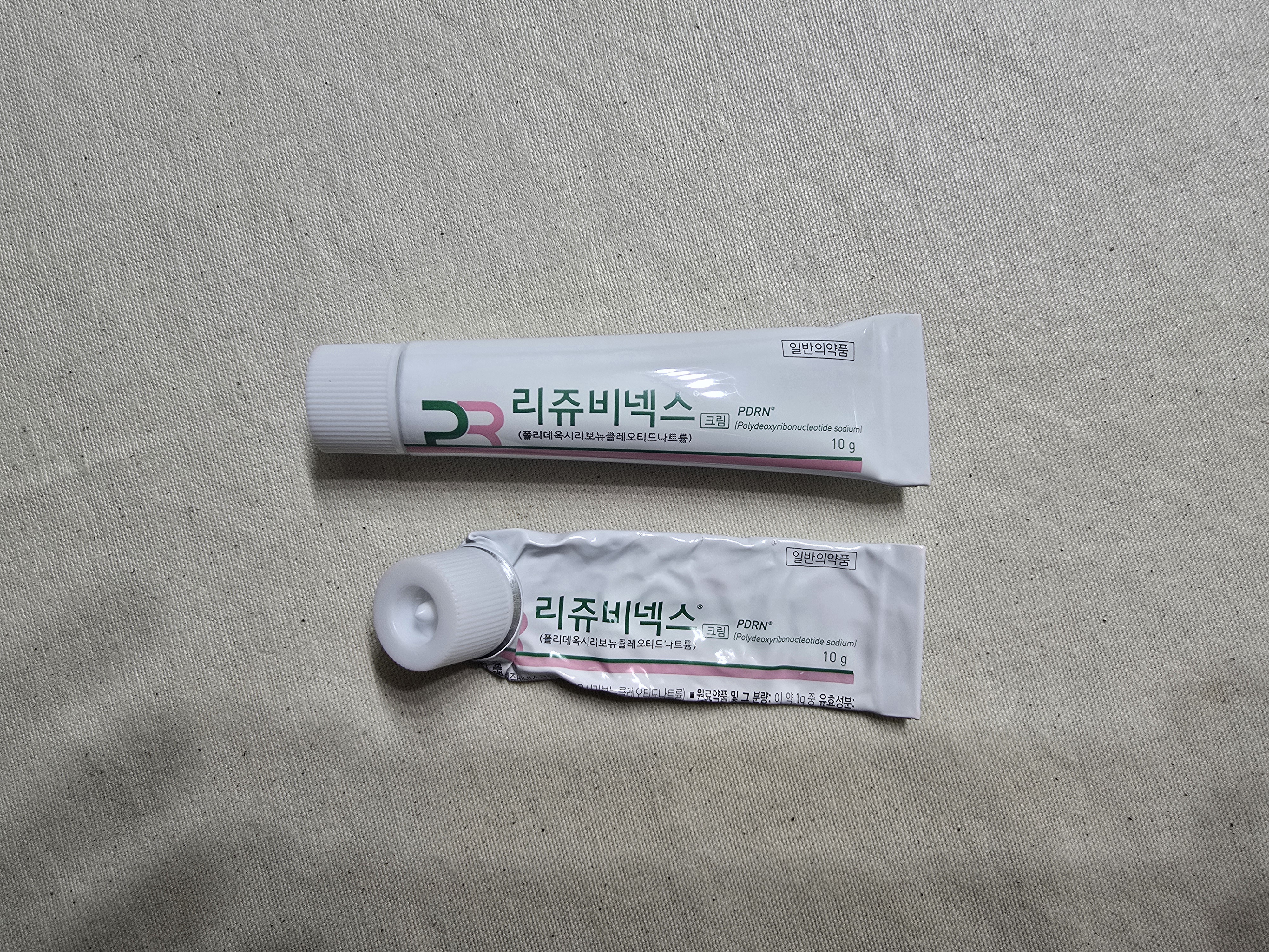 흰색 배경 위에 놓인 리쥬비넥스 크림 두 개가 나란히 놓여 있는 이미지.
한쪽은 사용 중인 주름진 튜브, 다른 하나는 새 제품 상태로,
약국 스킨케어템 리쥬비넥스 크림의 실제 제품 형태를 보여주는 사진