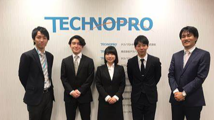 테크노 프로라고 적혀있는 벽면앞에 사람 5명이 정장을 입고 서있다.