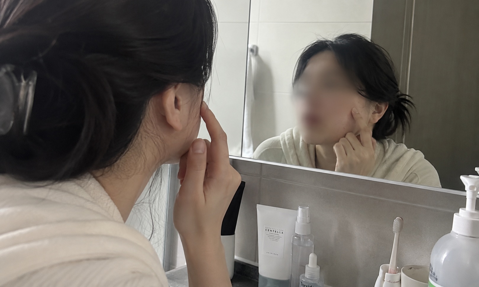 거울을 보며 볼의 좁쌀처럼 오돌토돌한 피부결을 확인하는 모습