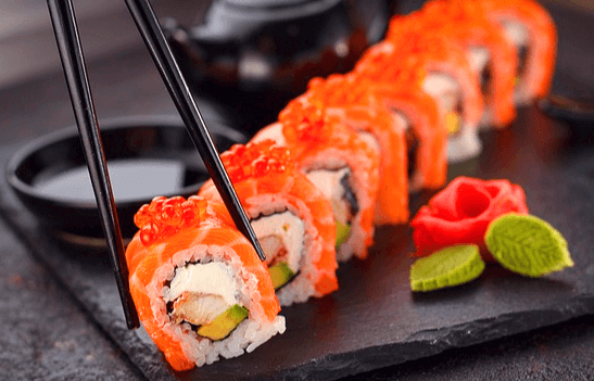 네모난 검정색 접시가 있다. 접시 위에는 연어와 연어알이 올려진 스시가 한줄 있다.